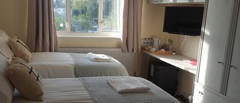 A bedroom with two beds, a desk with a computer, and a window with curtains.