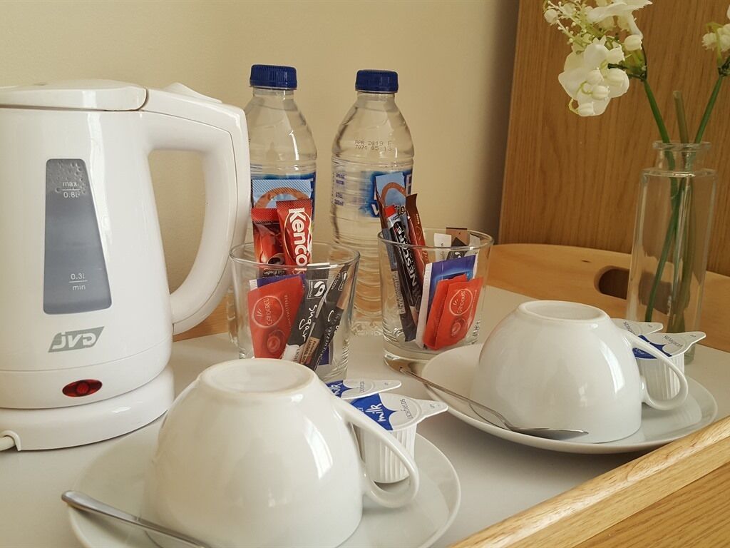 A table with a coffee maker, two bottles of water, a vase with flowers, and two cups with saucers.