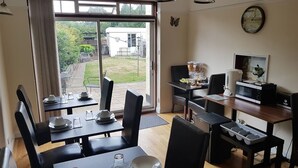 A dining area with a view of the garden, a kitchen area with appliances, and a dining table set for four. - Kathleen House (Enfield)