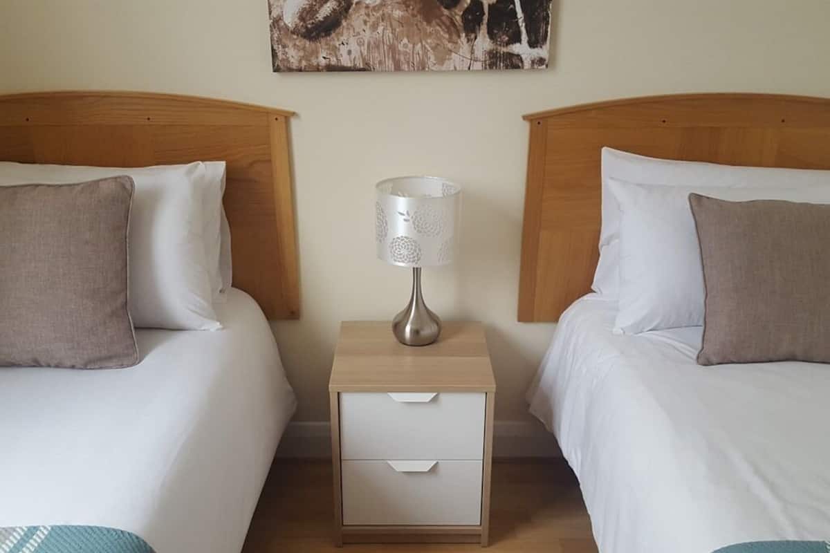 Ein Hotelzimmer mit zwei Einzelbetten, einem Nachttisch mit Lampe und einem Bild an der Wand.