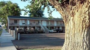 A motel with a two-story structure, a covered parking area, and a large tree in the foreground. - Gunnison Inn (Gunnison)