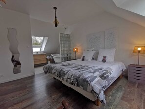 A bedroom with a large bed, a wooden dresser, a white chair, a glass shower enclosure, and a skylight. - Les Chambres de Capucine (Carcagny)