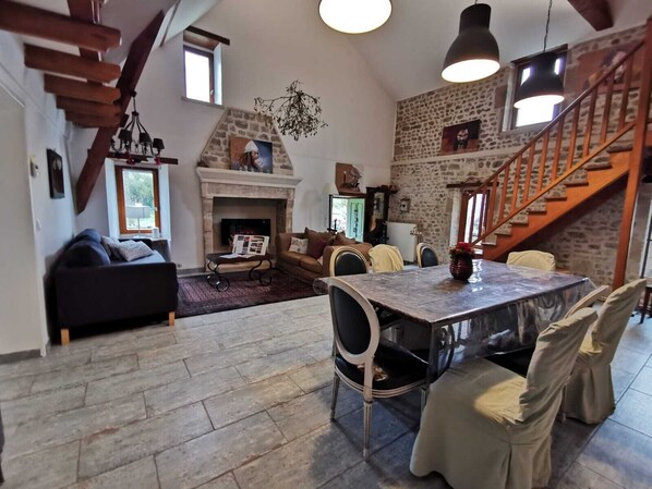 A cozy living room with a fireplace, a dining table, and a staircase. - Les Chambres de Capucine (Carcagny)