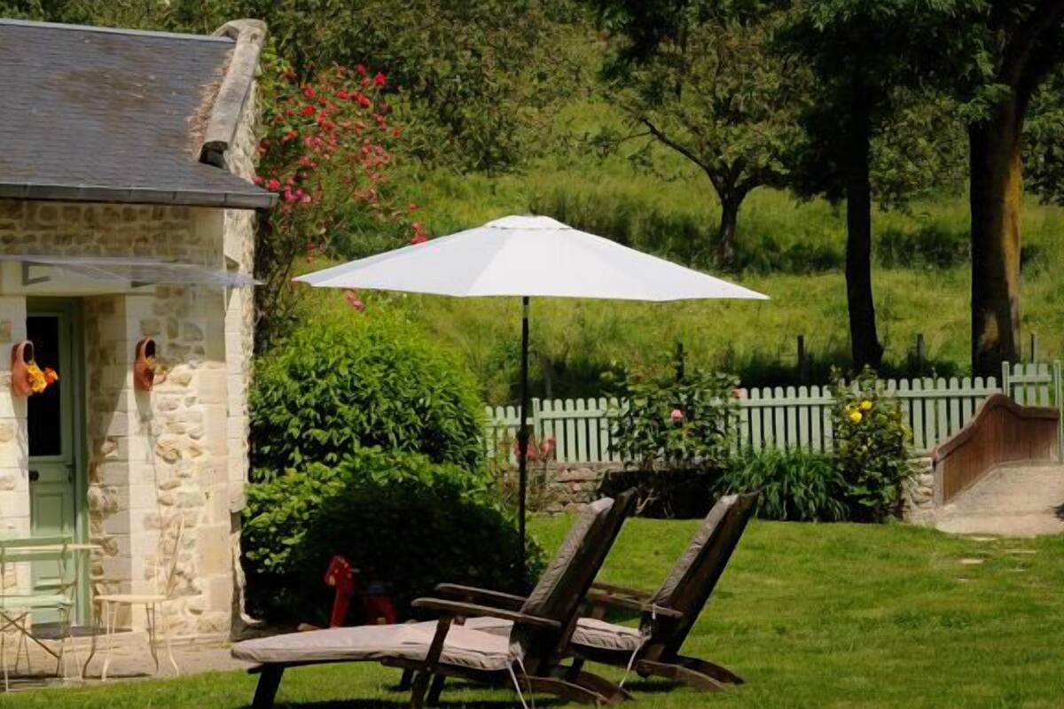 Ein Steinhaus mit einer kleinen Terrasse, einem weißen Sonnenschirm und Gartenmöbeln.