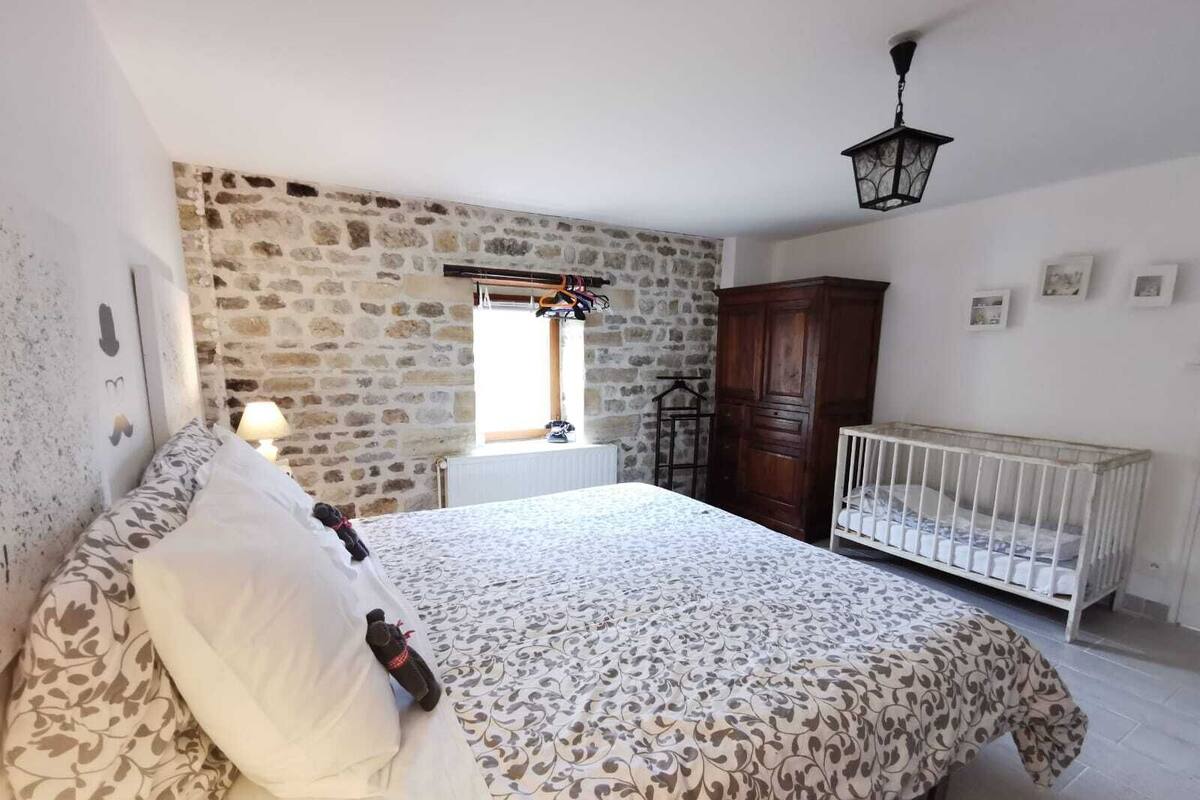 Ein Schlafzimmer mit einer Steinwand, einem Holzschrank, einem Babybett und einem Bett mit gemusterten Bettbezügen.