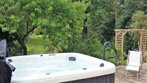 A hot tub in a garden with a wooden pergola and a white chair. - Les Chambres de Capucine (Carcagny)