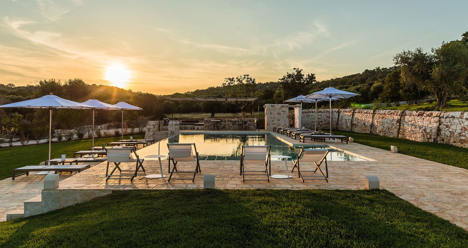 Ein Poolbereich mit Liegestühlen und Sonnenschirmen, umgeben von Steinmauern und viel Grün.