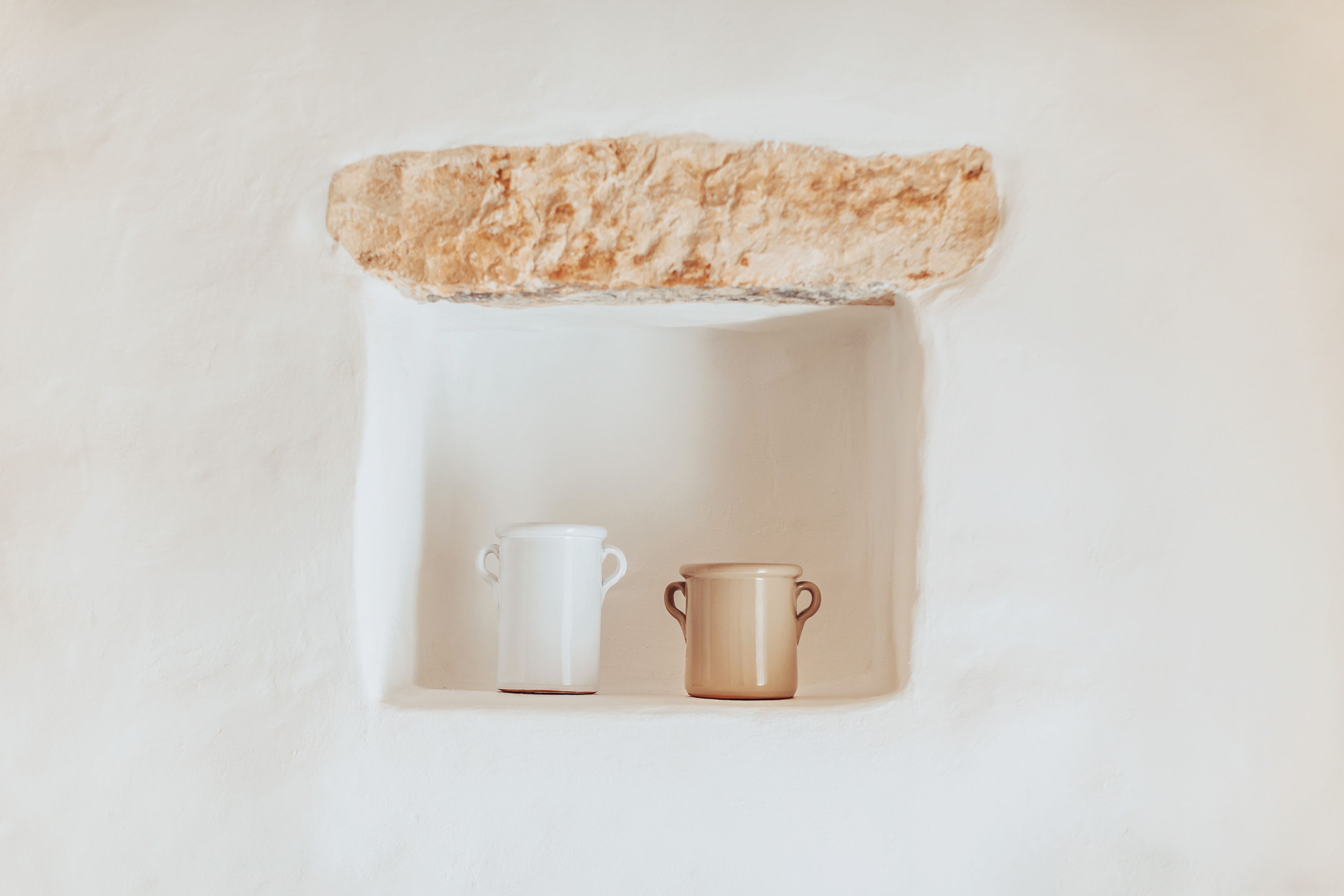 Una estantería blanca con dos tazas de cerámica, una blanca y otra marrón.