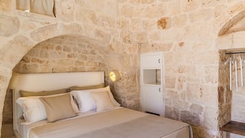 A bedroom with a stone wall, a bed with white linens, a nightstand, and a wall-mounted light.