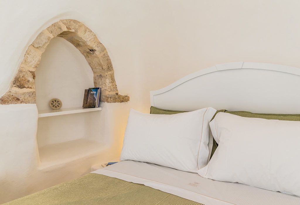 A bed with white bedding, a stone archway, and a shelf with a book and a decorative item.