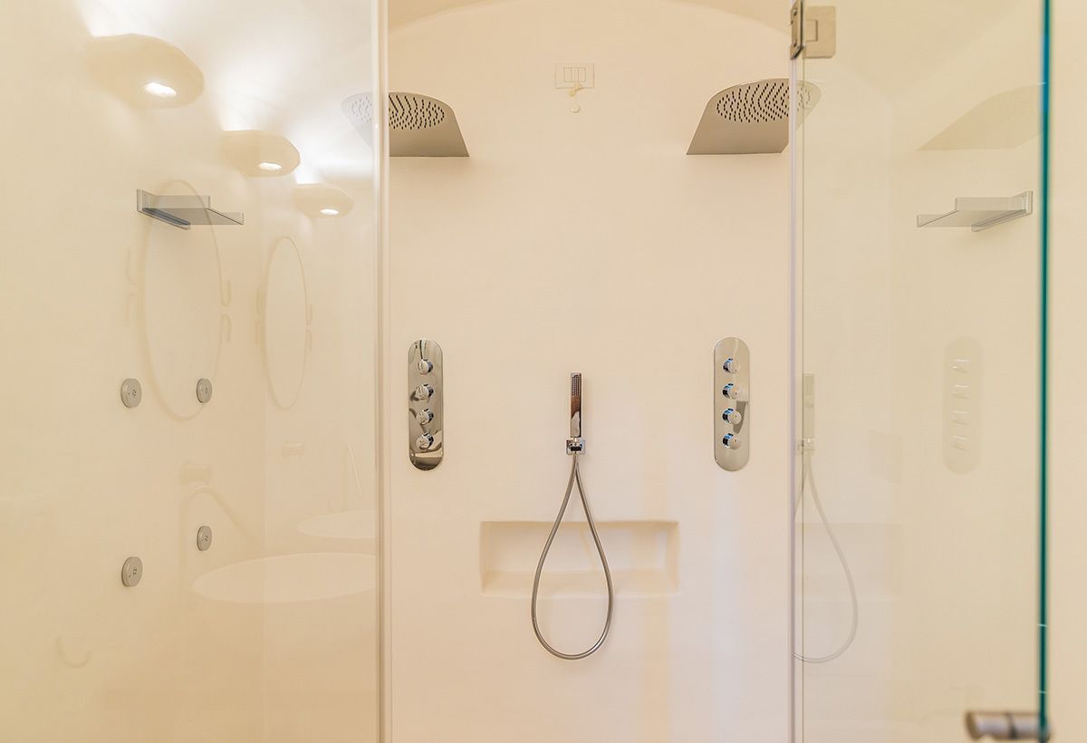A modern bathroom with a glass shower enclosure, a handheld showerhead, and a wall-mounted control panel.