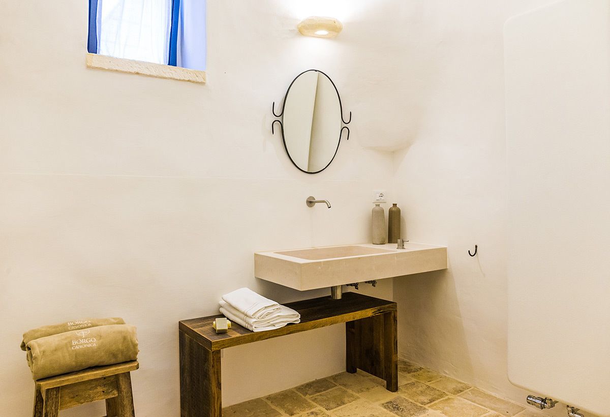 A bathroom with a white sink, a wooden stool with towels, and a mirror on the wall.