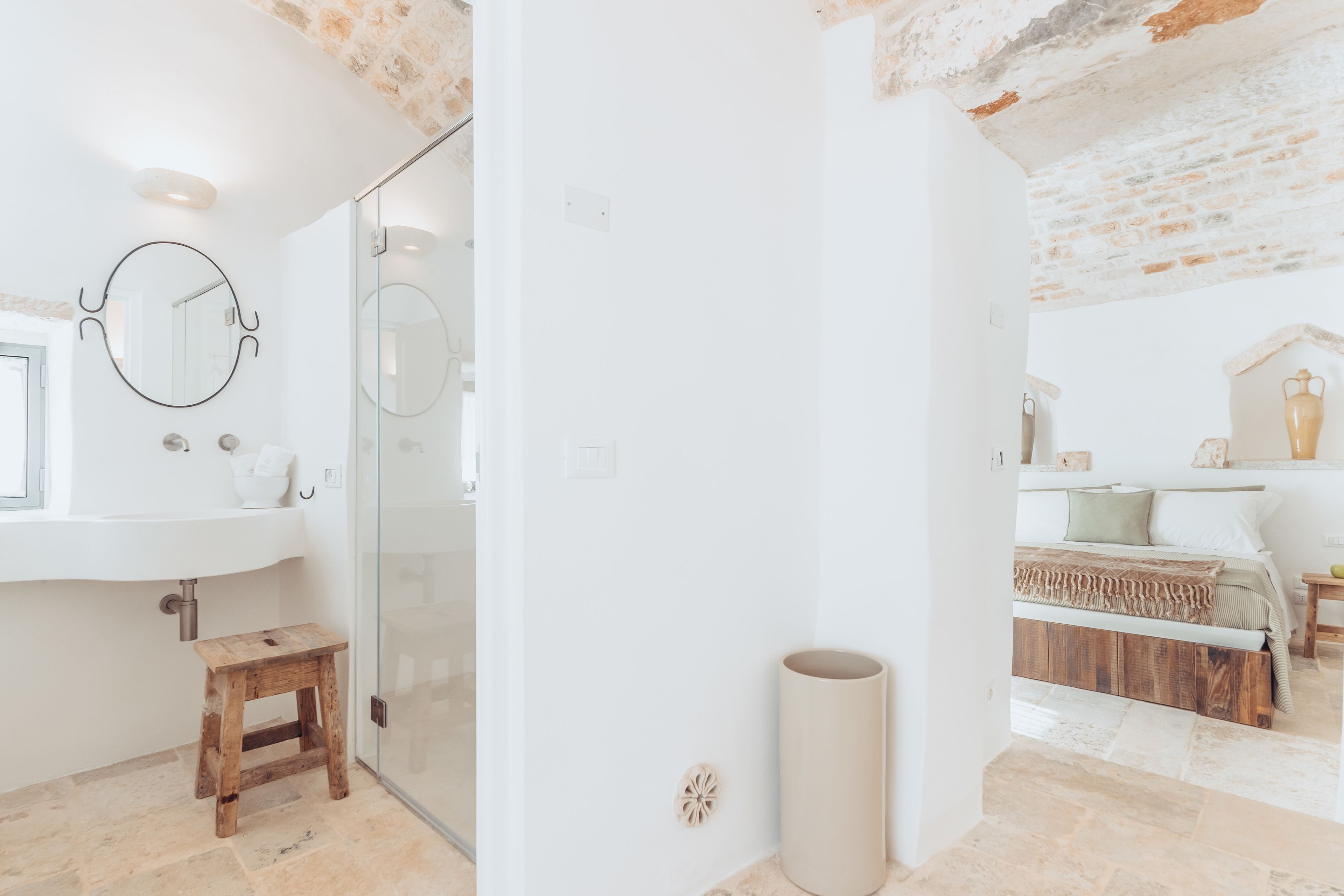 Un baño con cabina de ducha de vidrio, un taburete de madera y un lavamanos blanco con espejo.