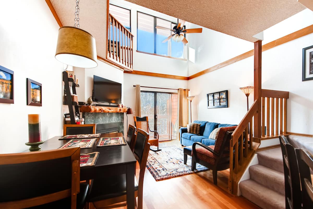 A spacious living area with a dining table, chairs, a blue sofa, and a staircase.