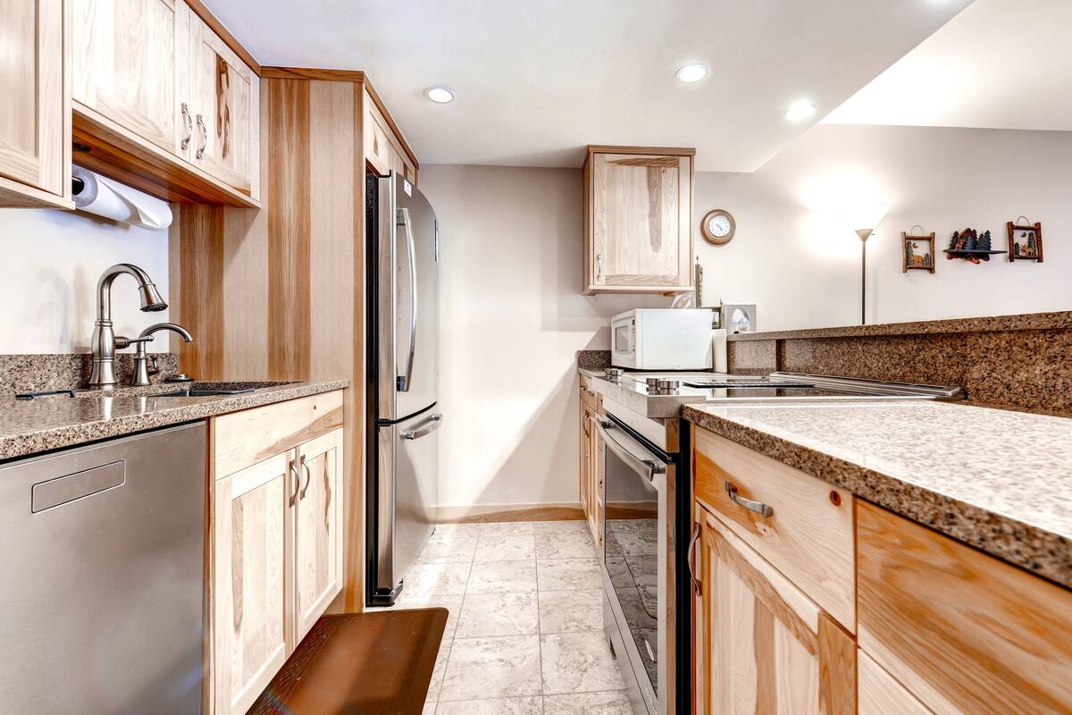 A modern kitchen with wooden cabinets, stainless steel appliances, granite countertops, and a built-in oven.