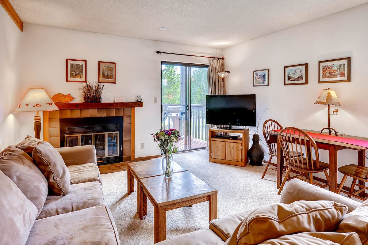 A living room with a sofa, coffee table, fireplace, TV, dining table, chairs, and artwork on the walls.