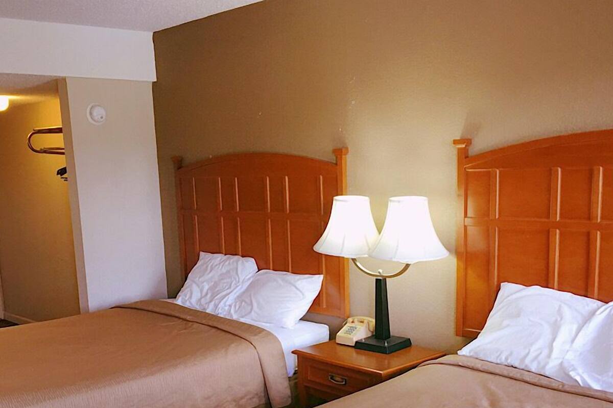 A hotel room with two beds, each with a wooden headboard, a bedside table with a lamp, and a telephone.