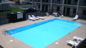 A rectangular pool with a blue interior, surrounded by white lounge chairs and a black fence. - Travelers Inn (Elizabethton)