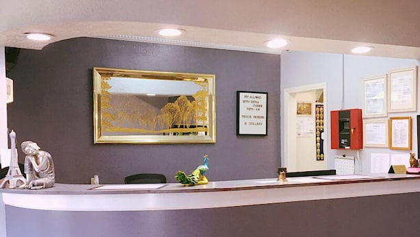 A reception desk with a framed landscape painting, a small statue, and a sign about parking charges. - Travelers Inn (Elizabethton)