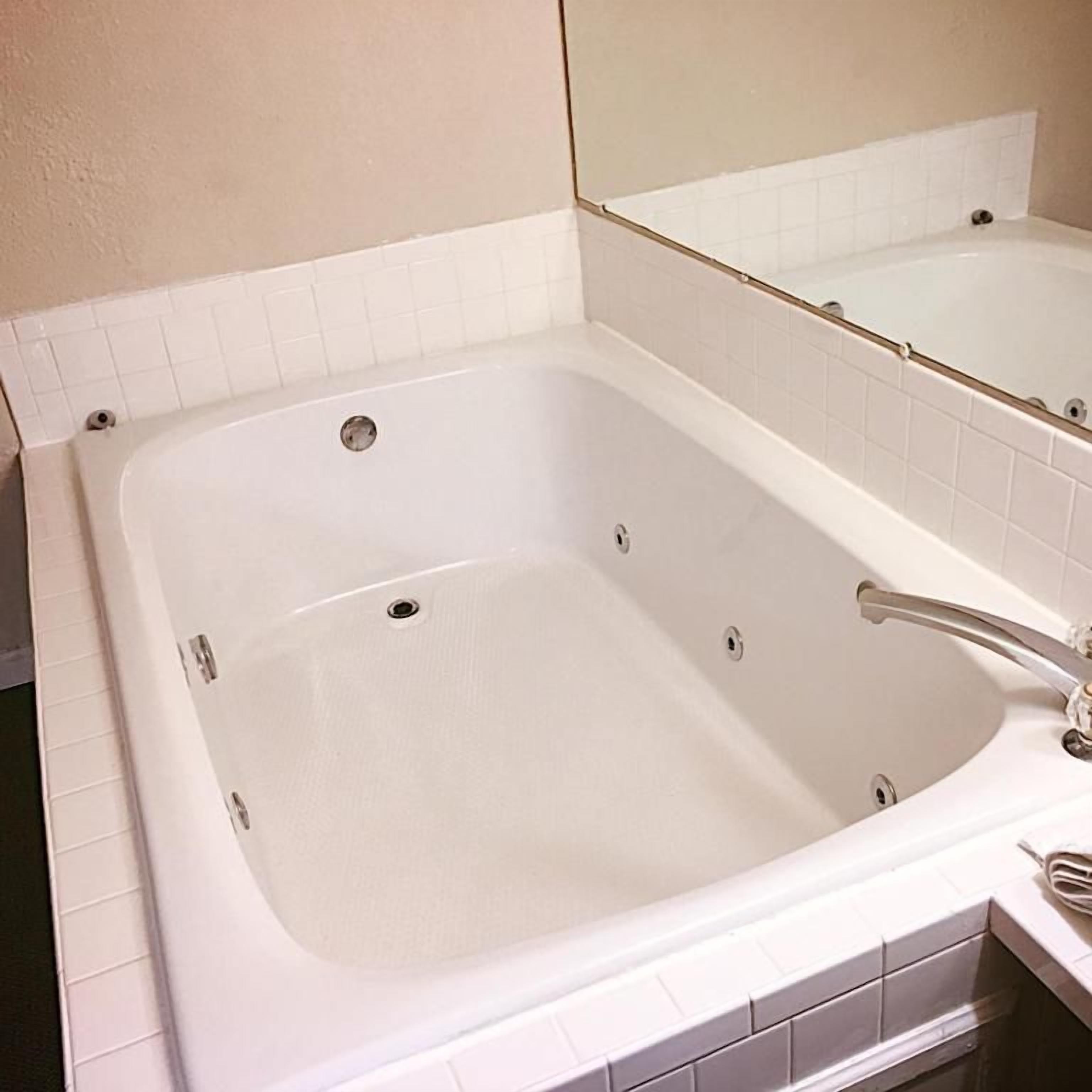 A white bathtub with a chrome faucet, a mirror above it, and a tiled wall.