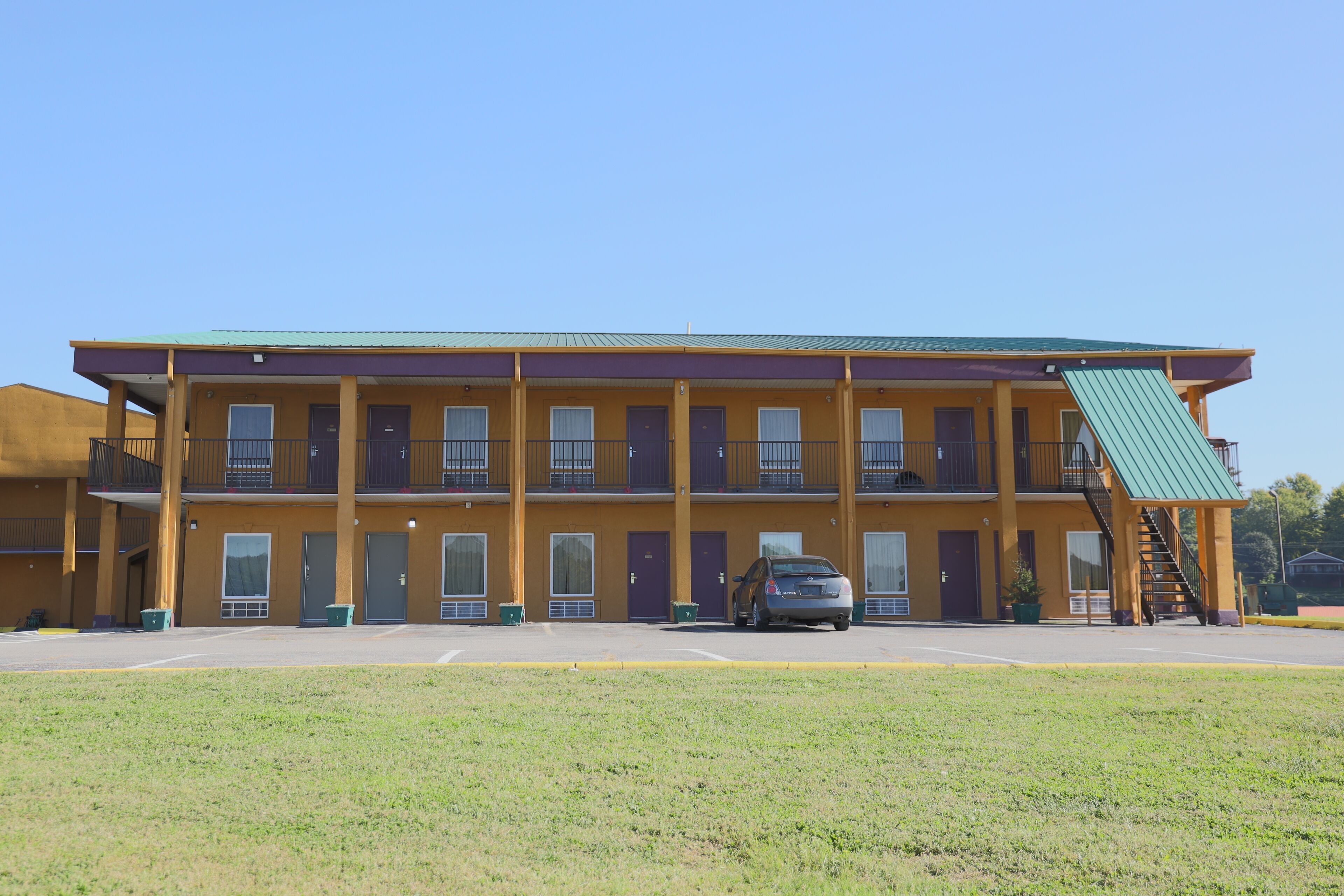 A motel with a two-story structure, a car parked in front, and a green awning over the entrance.