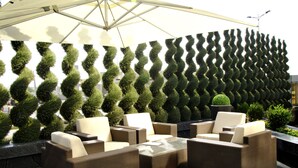 An outdoor seating area with wicker furniture and a patterned hedge wall.