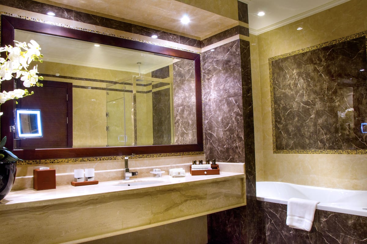 Une salle de bain avec un grand miroir, un lavabo, une baignoire et un vase rempli de fleurs.