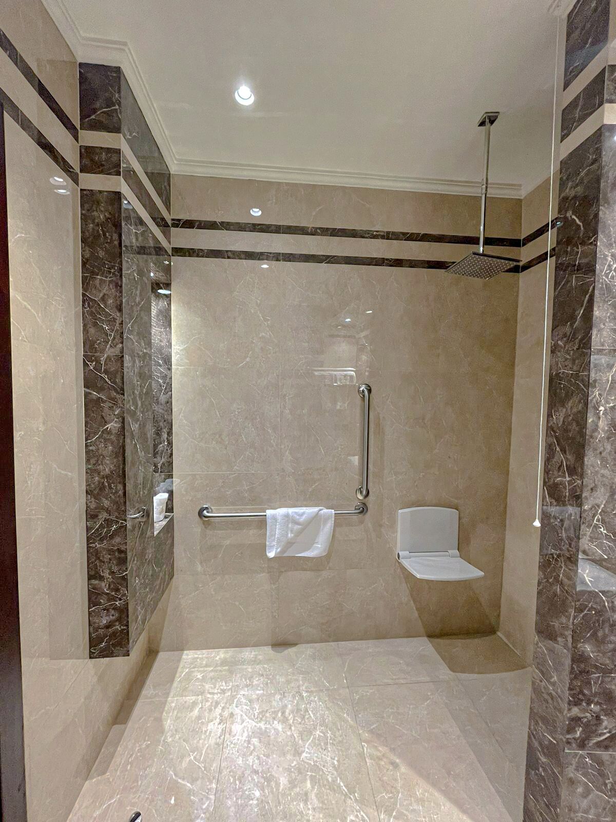 Un bagno moderno con doccia a filo pavimento, pareti in marmo e un porta asciugamani.