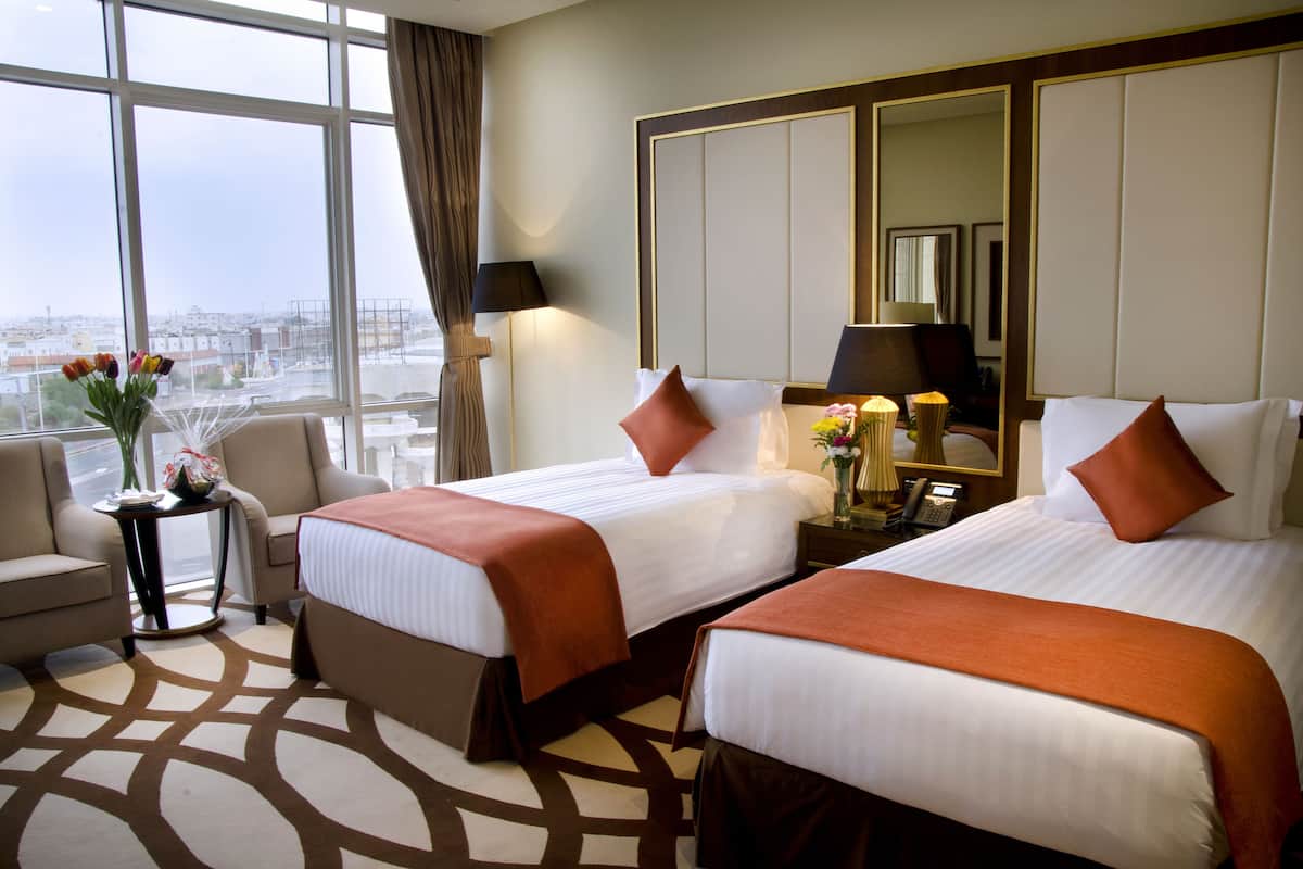 Une chambre d’hôtel avec deux lits, un coin salon, une grande fenêtre donnant sur un beau paysage et un miroir au mur.
