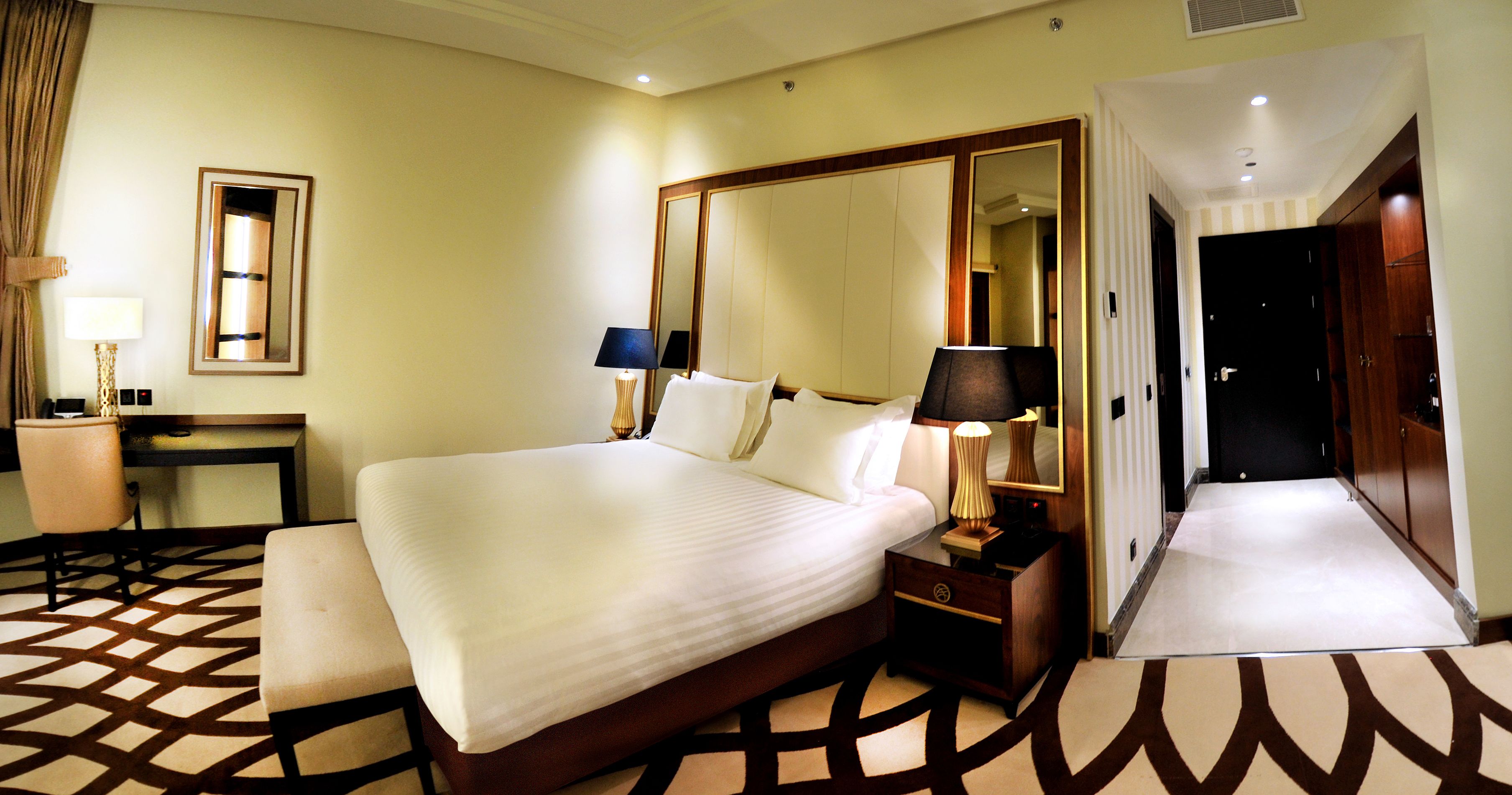 Una habitación de hotel con una cama grande, lámparas de noche, un escritorio y un espejo.