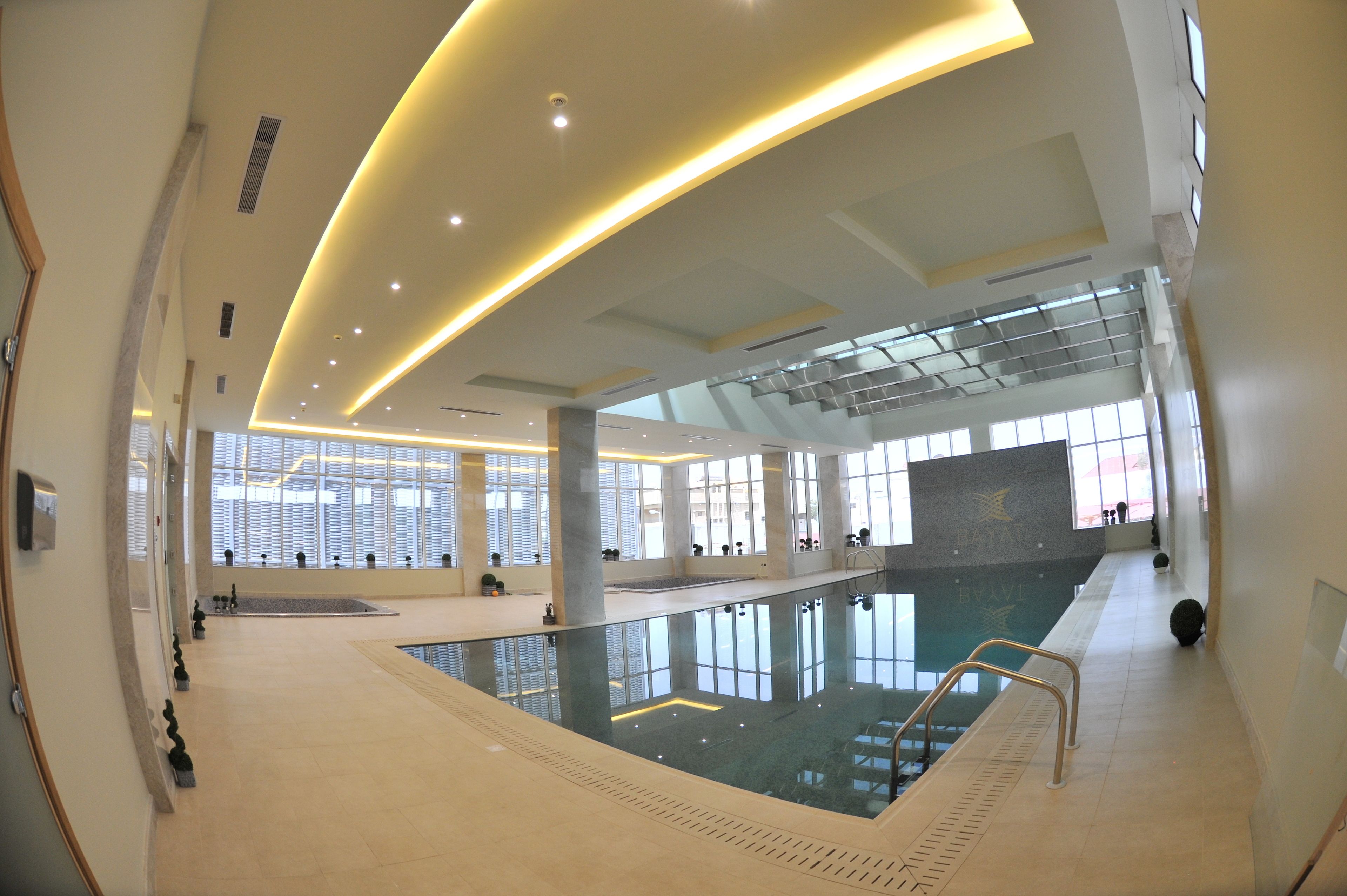 Una piscina interior moderna con paredes de vidrio transparente, una plataforma de clavados central y un diseño espacioso.