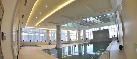 Una piscina interior moderna con paredes de vidrio transparente, una plataforma de clavados central y un diseño espacioso.