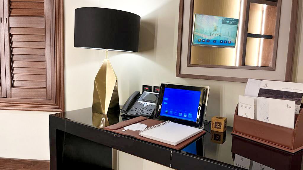 A hotel reception desk with a laptop, telephone, and framed picture on the wall.
