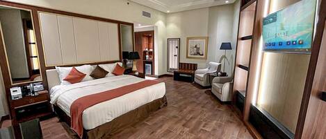 A hotel room with a large bed, a desk, a chair, a TV, and a wardrobe.