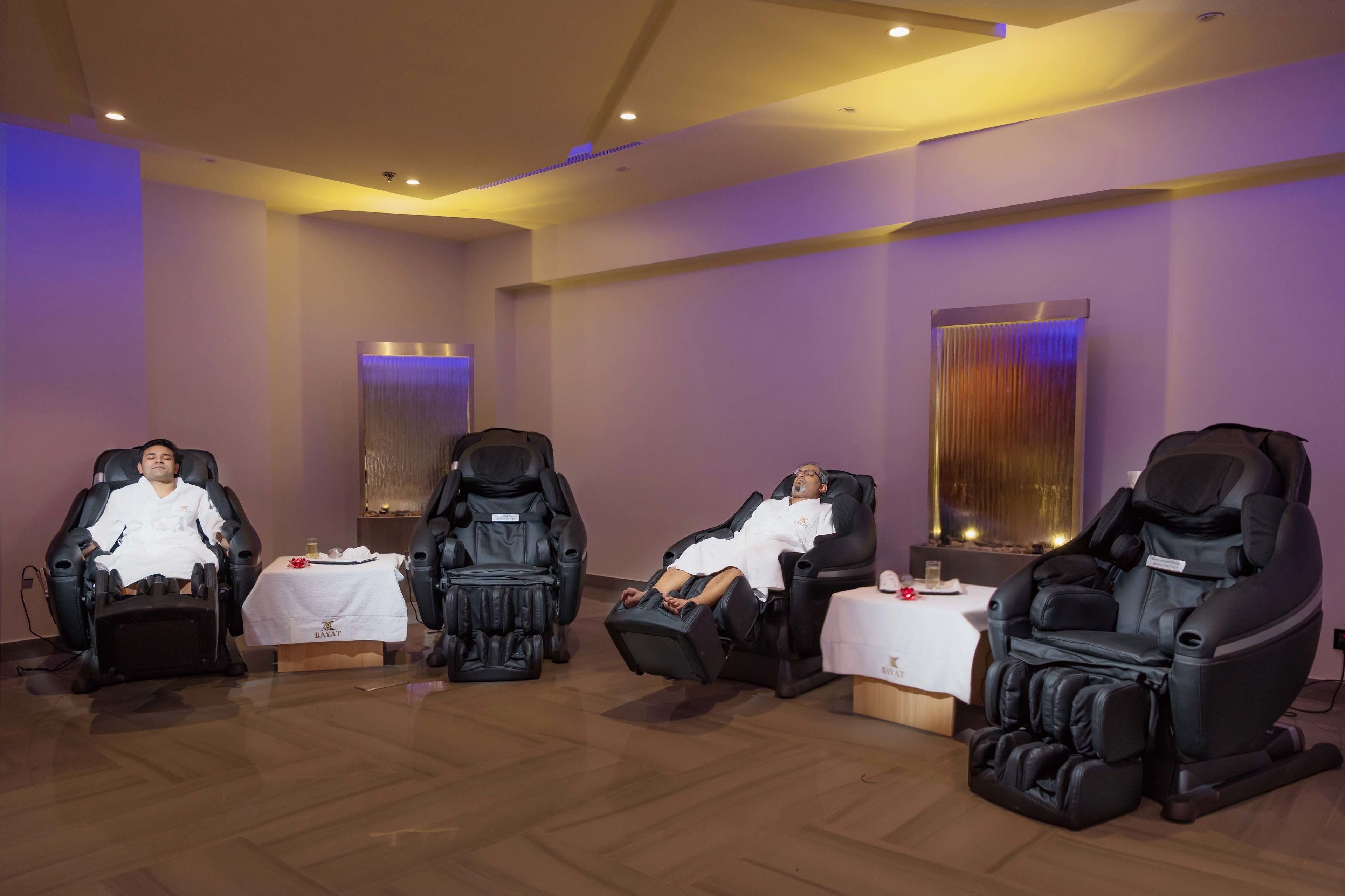 A room with four massage chairs, a small table with a white tablecloth, and a decorative water feature.