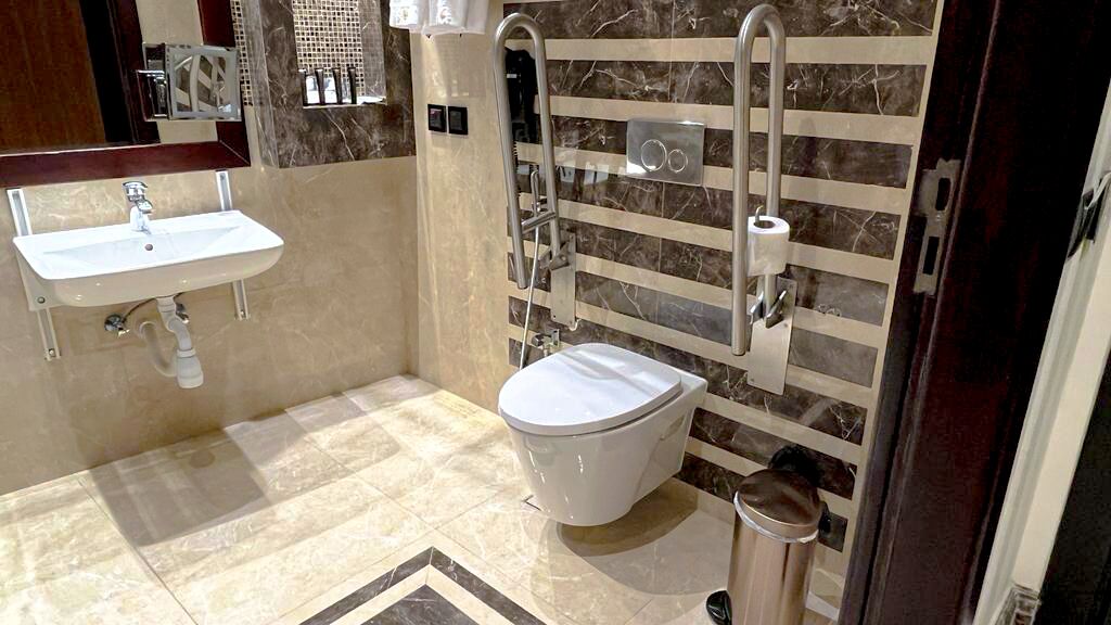 A bathroom with a white sink, a toilet, and a handrail.