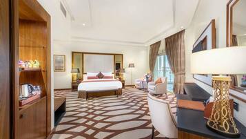 A hotel room with a large bed, a desk with a lamp, a chair, a wardrobe, and a large window with curtains.