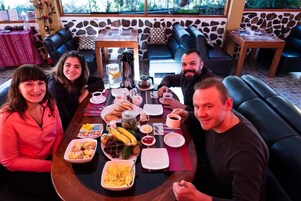 Un grupo de personas sentadas alrededor de una mesa con diversos platos y bebidas, en una sala con paredes de piedra y asientos de cuero.