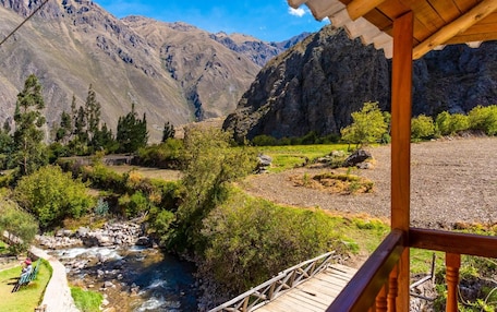 A mountain landscape with a river, trees, and a wooden bridge.