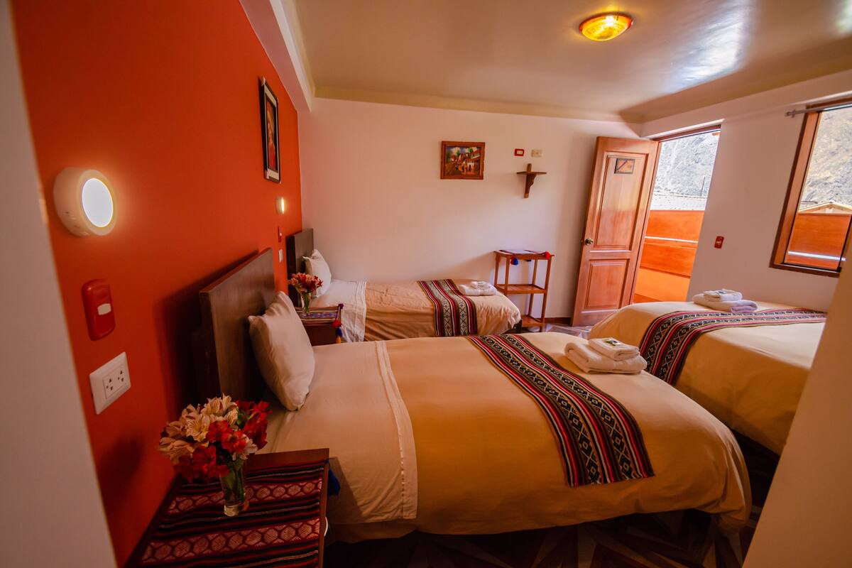Une chambre d’hôtel avec deux lits, une petite table ornée d’un vase de fleurs, une chaise en bois et une fenêtre donnant sur un paysage agréable.