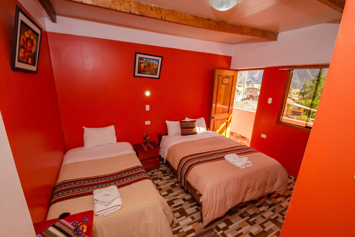 Une chambre avec deux lits, des murs rouges, un plafond en bois, une fenêtre donnant sur un paysage agréable et une porte.