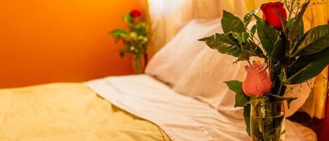 Una habitación de hotel con una cama, una mesita de noche con un florero y una ventana con cortinas.