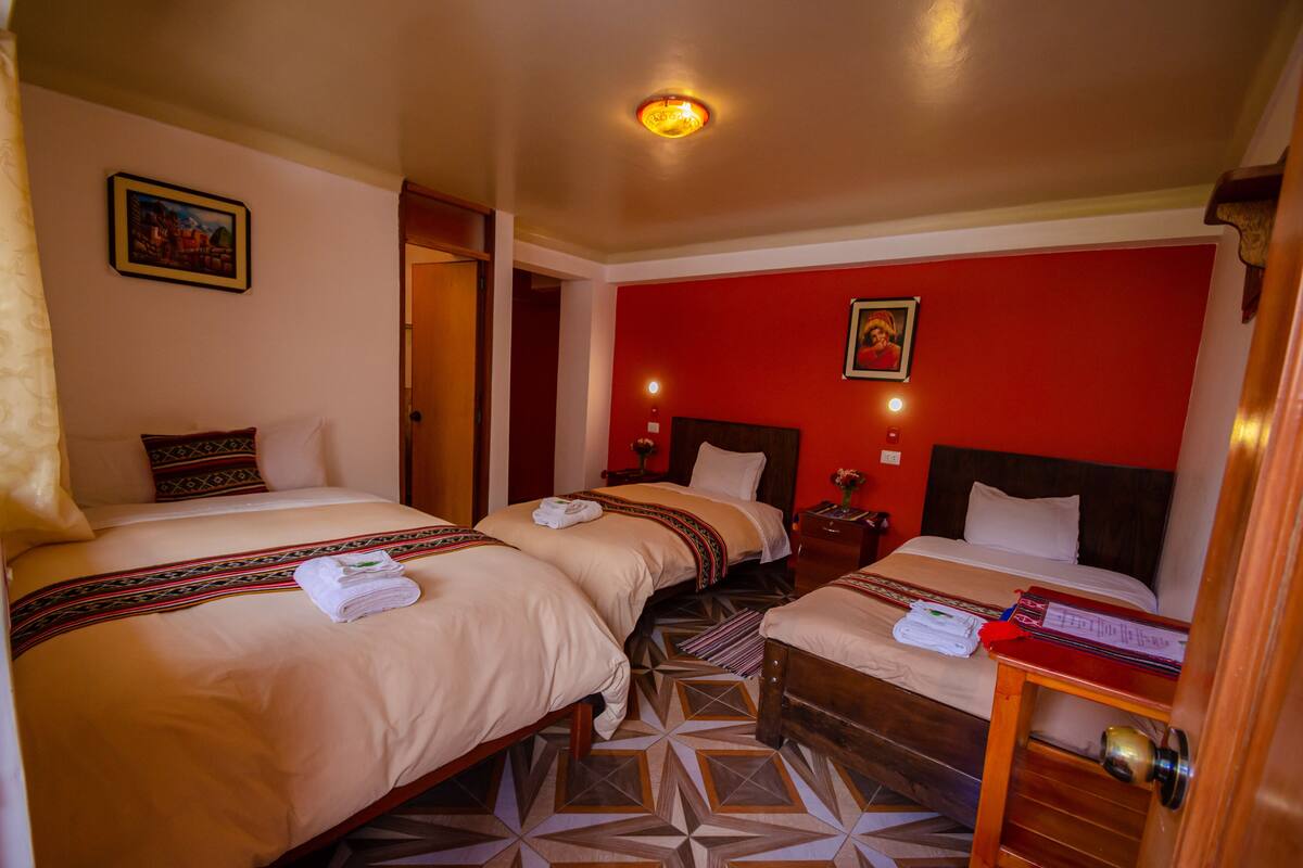 Une chambre d’hôtel avec deux lits, un mur d’accent rouge et un sol à motifs géométriques.