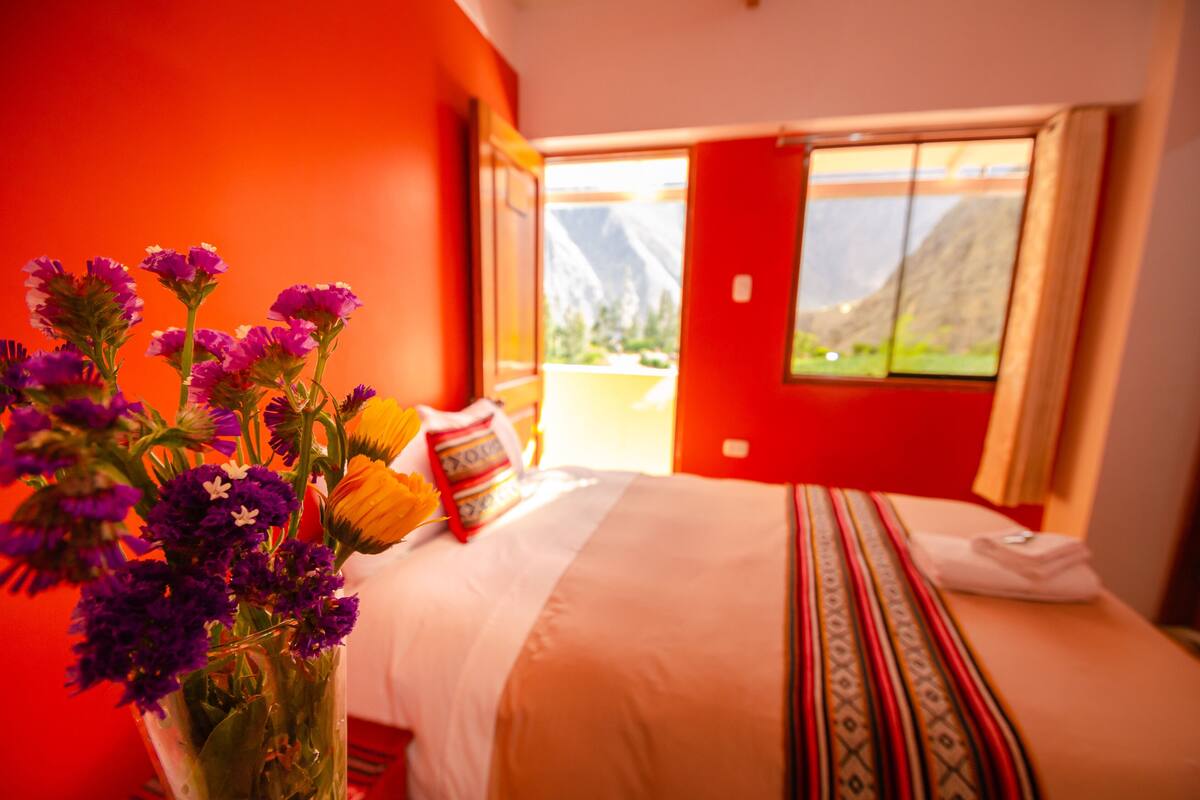 Une chambre d’hôtel avec un lit, un vase de fleurs et une vue sur la montagne par la fenêtre.