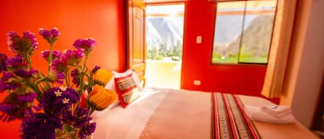 Ein Hotelzimmer mit Bett, Blumen in einer Vase und Blick auf die Berge durch das Fenster.