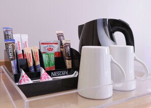 A coffee station with Nescafé products, two white mugs, and a black coffee maker on a clear surface. - StayEasy Century City (Cape Town)