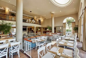 A spacious hotel lobby with multiple dining areas, high ceilings, and large windows. - StayEasy Century City (Cape Town)