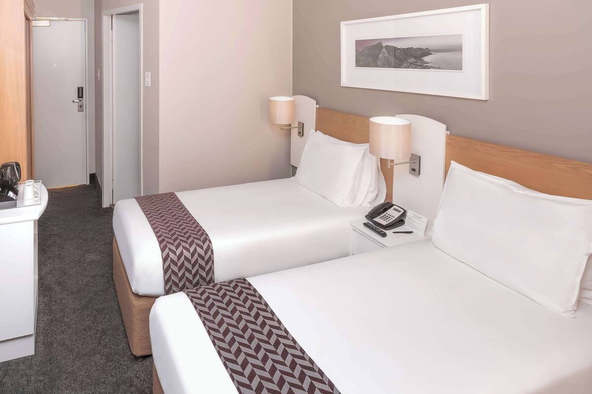Una habitación de hotel con dos camas, un escritorio, un teléfono y un cuadro en la pared.