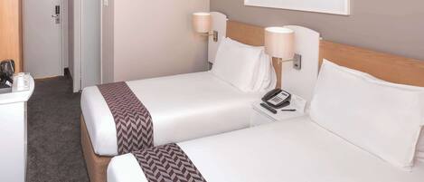 A hotel room with two beds, a desk, a phone, and a framed picture on the wall.