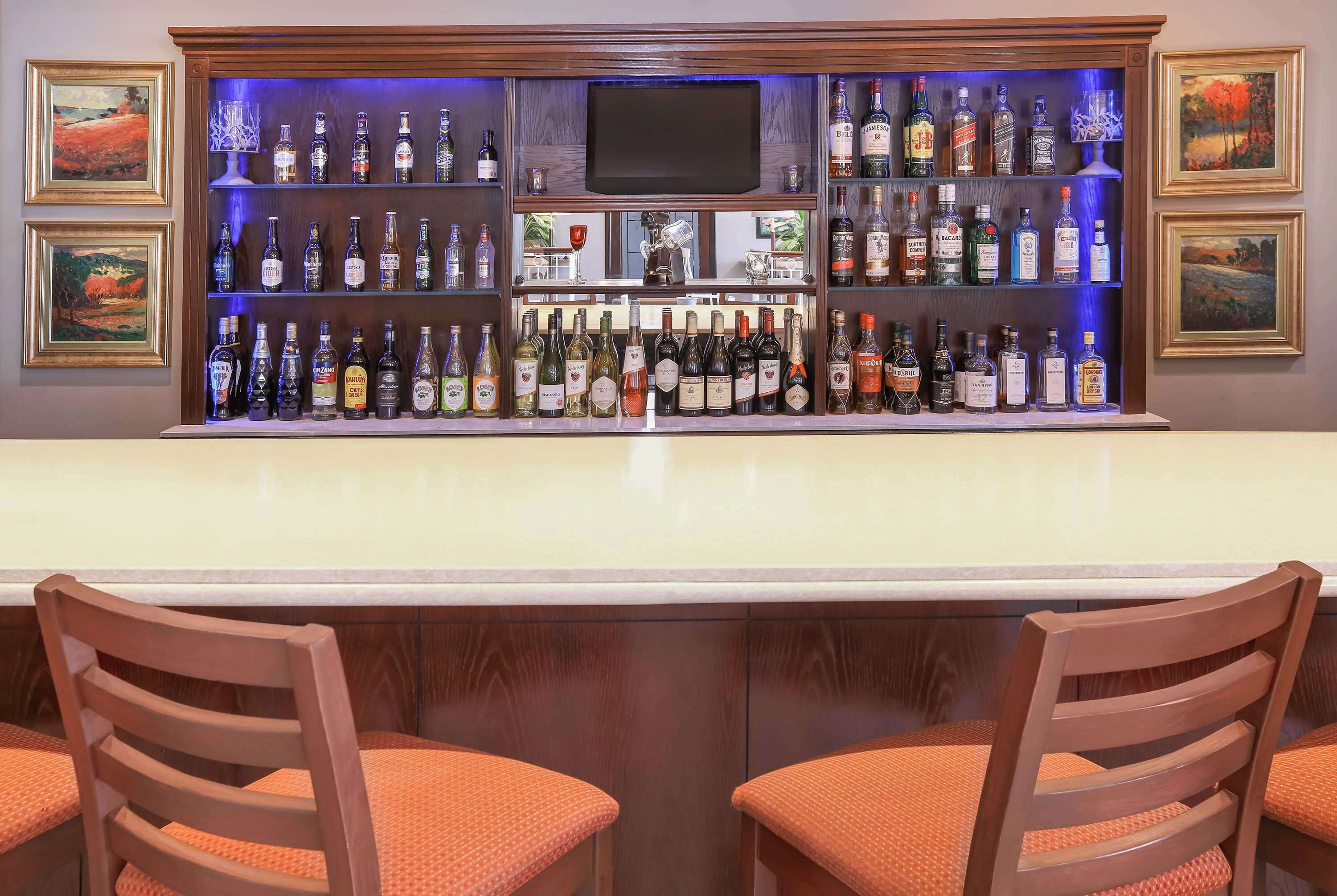 Una zona de bar con varias botellas de licor, un televisor y obras de arte enmarcadas en las paredes.